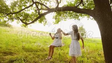 女朋友在一棵夏天的橡树<strong>下</strong>荡秋千，笑了起来。 女孩青少年一起玩在大自然和微笑。