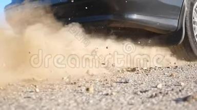 汽车车轮在运动开始时在沥青路上打滑。 小石头和泥土从轮胎下面飞出来
