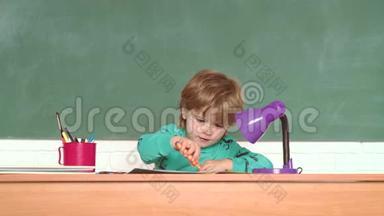 有趣的小男孩指着黑板。 学校的孩子。 开朗微笑的孩子在黑板前.. 教育。 小可爱