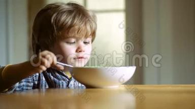 快乐的婴儿用勺子吃食物。 小男孩在厨房吃早餐。 快乐的小男孩勺子吃吃