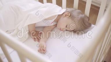 两岁的小女孩睡在铺着白色毯子的婴儿床上。 日间睡眠