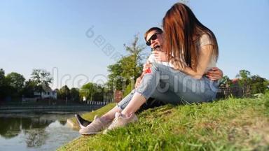 浪漫的夫妻喝咖啡，笑着坐在池塘附近的绿草上。 夫妻信任，爱情和幸福的概念