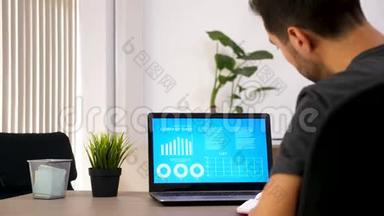 一个人在笔记本上写下笔记，同时看电脑屏幕上有动画数据