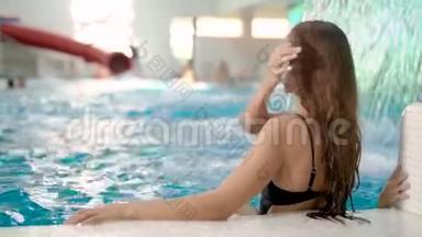 从一个漂亮的黑发女人坐在室内游泳池的背后观看。