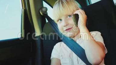 有趣的女孩6岁打电话，坐在车后座。 用<strong>安全带</strong>系好