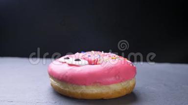 特写镜头围绕着一个美味的釉粉色甜甜圈，上面有五颜六色的薯片，眼睛在灰色上慢慢旋转
