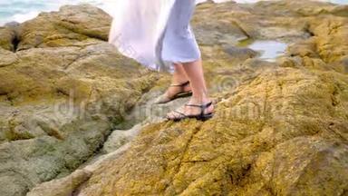 特写镜头。 女人穿着凉<strong>鞋</strong>`腿和一条长长的灰色裙子在低<strong>潮</strong>的岩石海岸上。