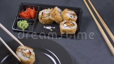 手拿筷子拿寿司.. 寿司卷在深色盘子上。 `是吃零食的时候