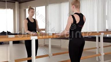 漂亮的体操运动员在一个有芭蕾车床和镜子的房间里做劈叉动作