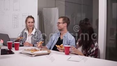 年轻的白种人同事午休时一起在办公室吃披萨。 笑，说话，玩得开心。 工作人员