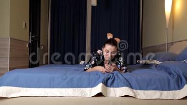 美丽的黑发女孩躺在床上用<strong>手机</strong>。 网上<strong>约会</strong>