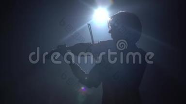 在一个黑暗的工作室里，一个音乐家在那里拉小提琴。 黑烟背景。 背面