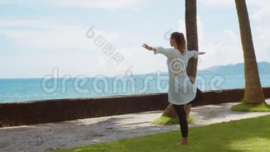 年轻的白种人女子在巴厘岛平静的海洋附近的海滩上练习瑜伽放松<strong>身心</strong>，背景优美