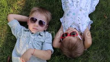 公园里的草地上躺着<strong>两个</strong>戴太阳镜的<strong>小孩子</strong>。 从顶部看。