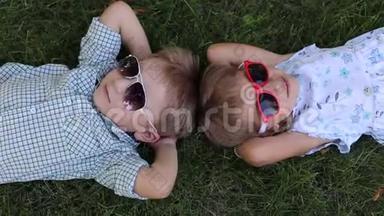 公园里的草地上躺着<strong>两个</strong>戴太阳镜的<strong>小孩子</strong>。 从顶部看。