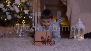 <strong>一个</strong>小男孩打开<strong>一个</strong>带礼物的盒子，高兴地躺在圣诞树附近的<strong>地板上</strong>。 高清高清