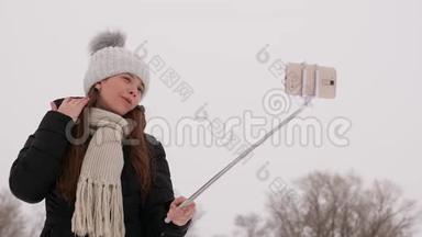 年轻女孩在智能手机和自粘上拍照，在冬季公园-圣诞节早上。 快乐的女孩走进来