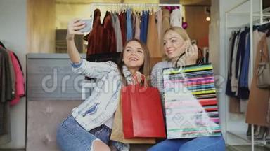 可爱的女孩子在女装精品店里用五颜六色的纸袋自拍`然后用智能手机观看