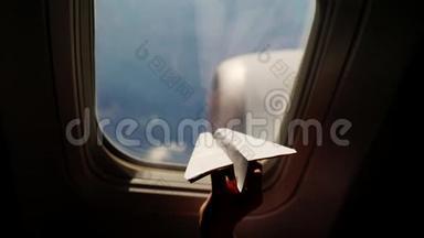 特写镜头。 一个孩子的手`小纸飞机在飞机窗口的背景下的剪影。 儿童