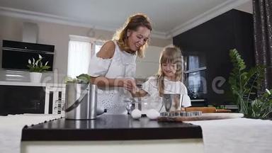 美丽的年轻母亲和她的小女儿把面粉倒进玻璃碗里，煮一个面团来烘焙。 美丽美丽