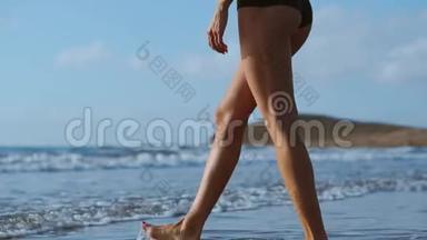 一个女人赤脚在海滩上行走，进入海洋的特写镜头。 慢动作稳定