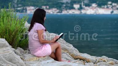 美丽的年轻女孩在海边读碑文和梦想。