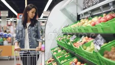 穿着休闲服装的迷人女孩正沿着水果排走，移动购物手推车，看着有机水果。