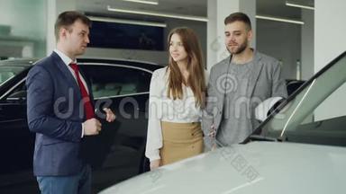 友好的汽车推销员正在和自信的年轻人谈论新车型，而漂亮的女人则在谈论