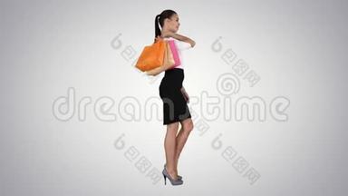 美丽的微笑女人，穿着正式的衣服，走着，在渐变的背景上带着五颜六色的购物袋。