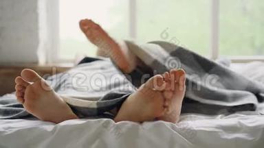 可爱的情侣躺在床上，躺在毯子下聊天，专注于赤脚触摸和抚摸对方