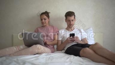 一对快乐<strong>的夫妻在</strong>家里<strong>躺在床上</strong>，用电脑和手机