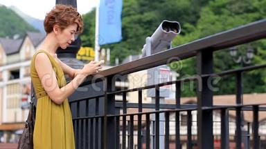 夏天，年轻可爱的女人站在街上，在城市背景下的智能手机上输入一条信息