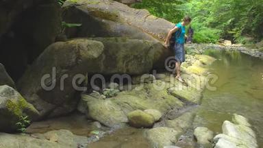 徒步旅行美丽的女人，带着背包，用智能手机在山河上拍照，大石头和绿色的苔藓。