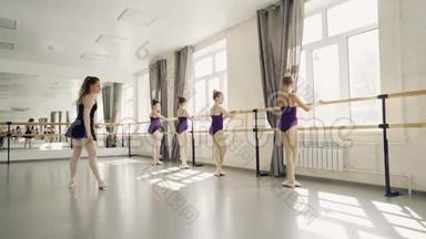 年轻的芭蕾舞演员在专业芭蕾舞演员严格的教师指导下在芭蕾舞酒吧练习腿部姿势
