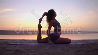 迷人的瑜伽女人在海边的垫子上锻炼。 混合瑜伽姿势。 清晨黄昏