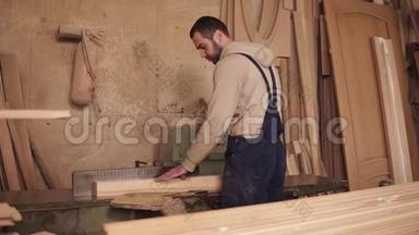 木匠把圆锯上木块的两侧剪开.. 木制刨花。 车间里满是