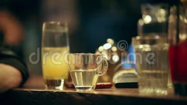 酒吧。 一个人从酒吧柜台喝含酒精的鸡尾酒。 一个端着水的茶杯站在柜台上