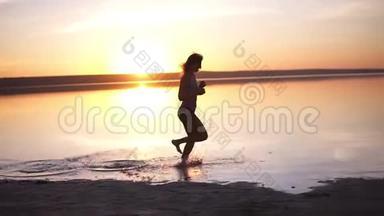 日落或日出背景下在水面上奔跑的女孩的剪影。 苗条的女孩跑得很快，离开了她