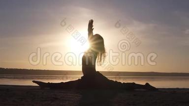 一位美丽的瑜伽女孩在海滩日出时的剪影。 哈努马纳萨纳，猴子姿势。 太阳落在尸体上