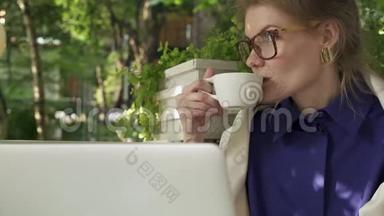 戴眼镜的嬉皮士女孩在她的笔记本电脑附近的<strong>夏日咖啡</strong>馆喝<strong>咖啡</strong>