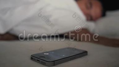 年轻人睡在床上，<strong>手机</strong>显示器上有<strong>闹钟</strong>。 现代技术