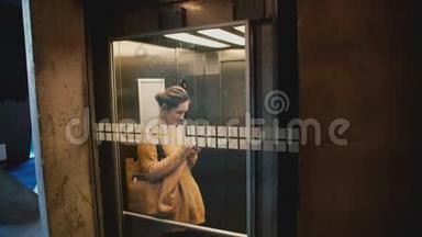 年轻快乐微笑的女人乘坐电梯与透明玻璃墙，步行出去使用智能手机购物应用程序在线。