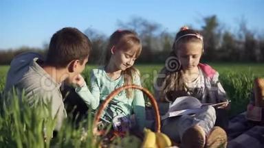 天气很好，刮风。 父亲带着两个女儿在一片绿色的田野上野餐。 小女孩在喂她爸爸