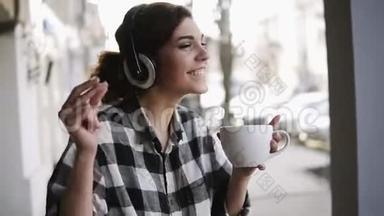 快乐，有趣的年轻女孩听着耳机里的<strong>音</strong>乐，手里拿着一杯咖啡跳舞。 模糊的<strong>街道</strong>