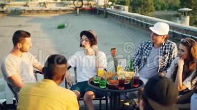 快乐的朋友在温暖的晴天坐在屋顶上聊天，喝柠檬水，桌上有<strong>零食</strong>和<strong>饮料</strong>