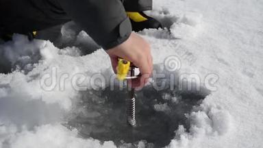 高加索人用冰螺钉在冰冻的湖面上钻冰。 快关门。 身体部分