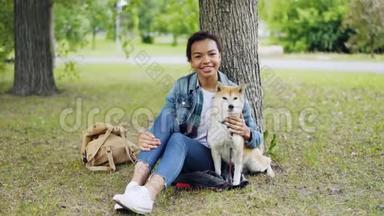 非洲裔美国女孩爱狗主人坐在公园的草地上与她美丽的宠物，微笑和看起来