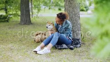 快乐的狗主人迷人的非裔美国女孩抚摸她的纯种狗，坐在公园的草坪上和它说话