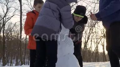 4个男孩慢动作在冬季公园堆雪人