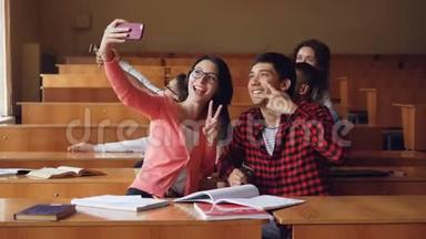 快乐<strong>的学生</strong>正<strong>在教室里</strong>自拍，坐<strong>在</strong>桌子旁，拿着智能手机。 现代技术
